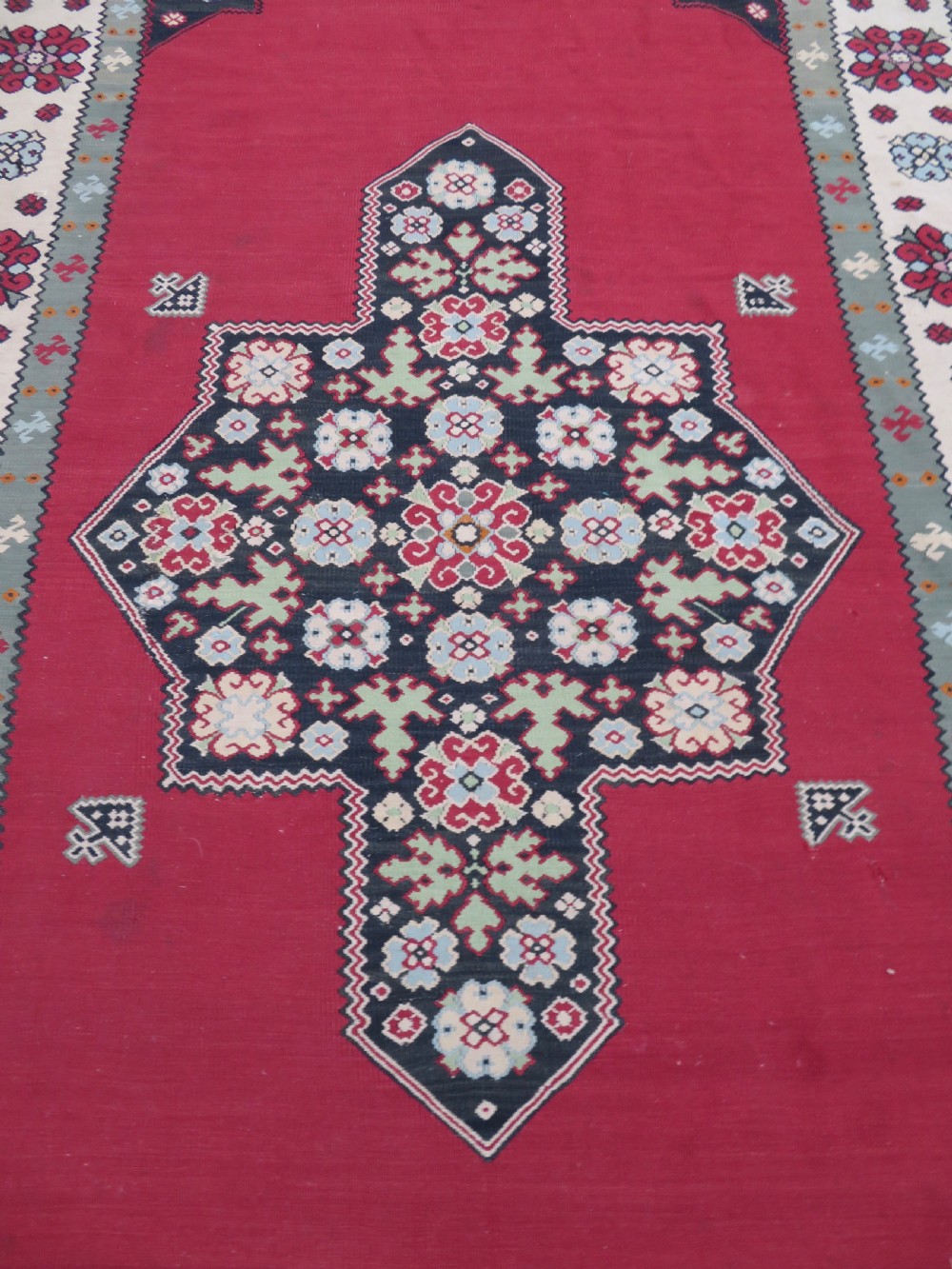 An antique flatweave Bessarabian wool rug featuring a red field with a central black and cream floral medallion, surrounded by a wide floral border and fringed edges. View IV