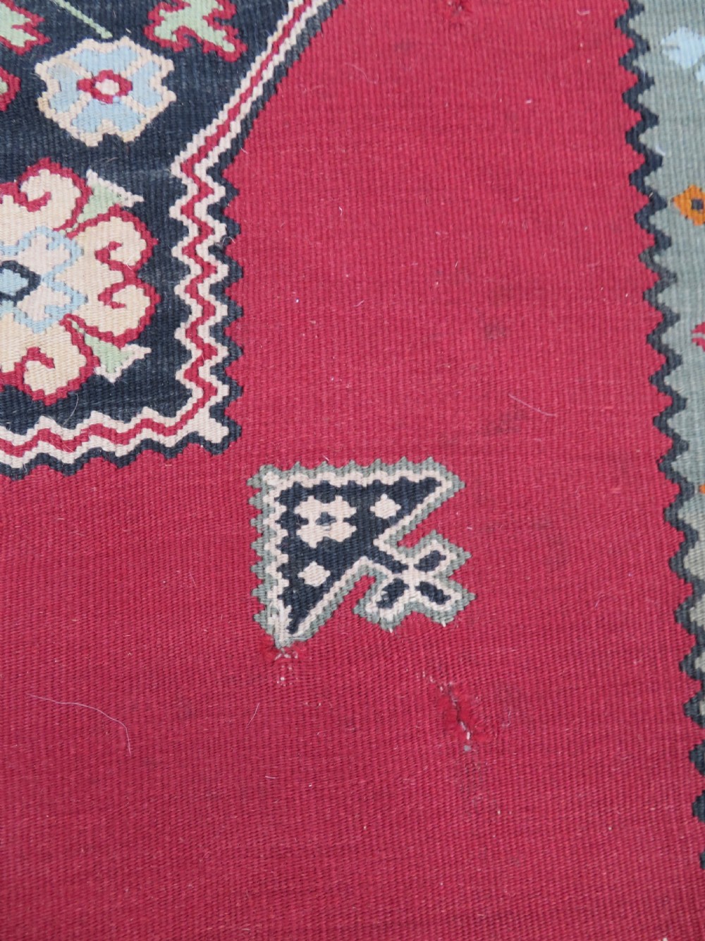 An antique flatweave Bessarabian wool rug featuring a red field with a central black and cream floral medallion, surrounded by a wide floral border and fringed edges. View VI