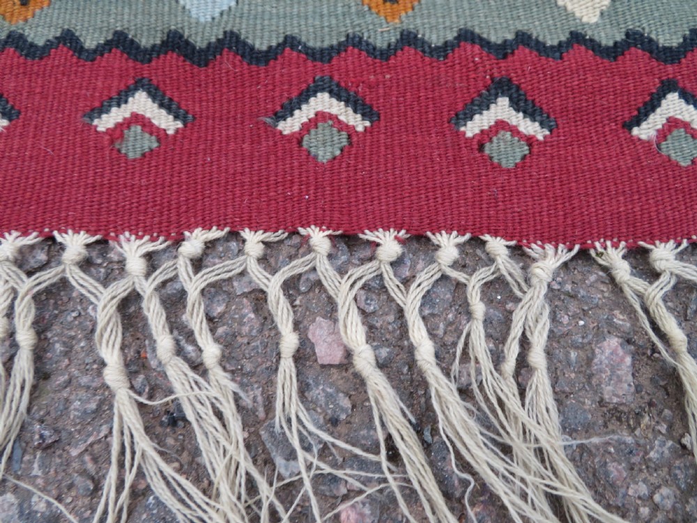An antique flatweave Bessarabian wool rug featuring a red field with a central black and cream floral medallion, surrounded by a wide floral border and fringed edges. View VIII