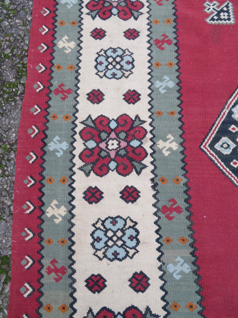 An antique flatweave Bessarabian wool rug featuring a red field with a central black and cream floral medallion, surrounded by a wide floral border and fringed edges. View X