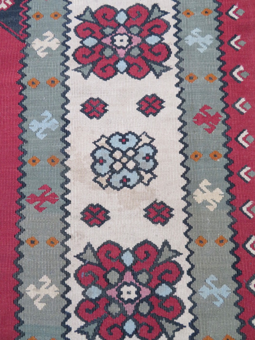 An antique flatweave Bessarabian wool rug featuring a red field with a central black and cream floral medallion, surrounded by a wide floral border and fringed edges. View XIII