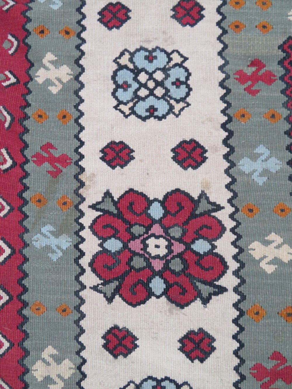 An antique flatweave Bessarabian wool rug featuring a red field with a central black and cream floral medallion, surrounded by a wide floral border and fringed edges. View XIV