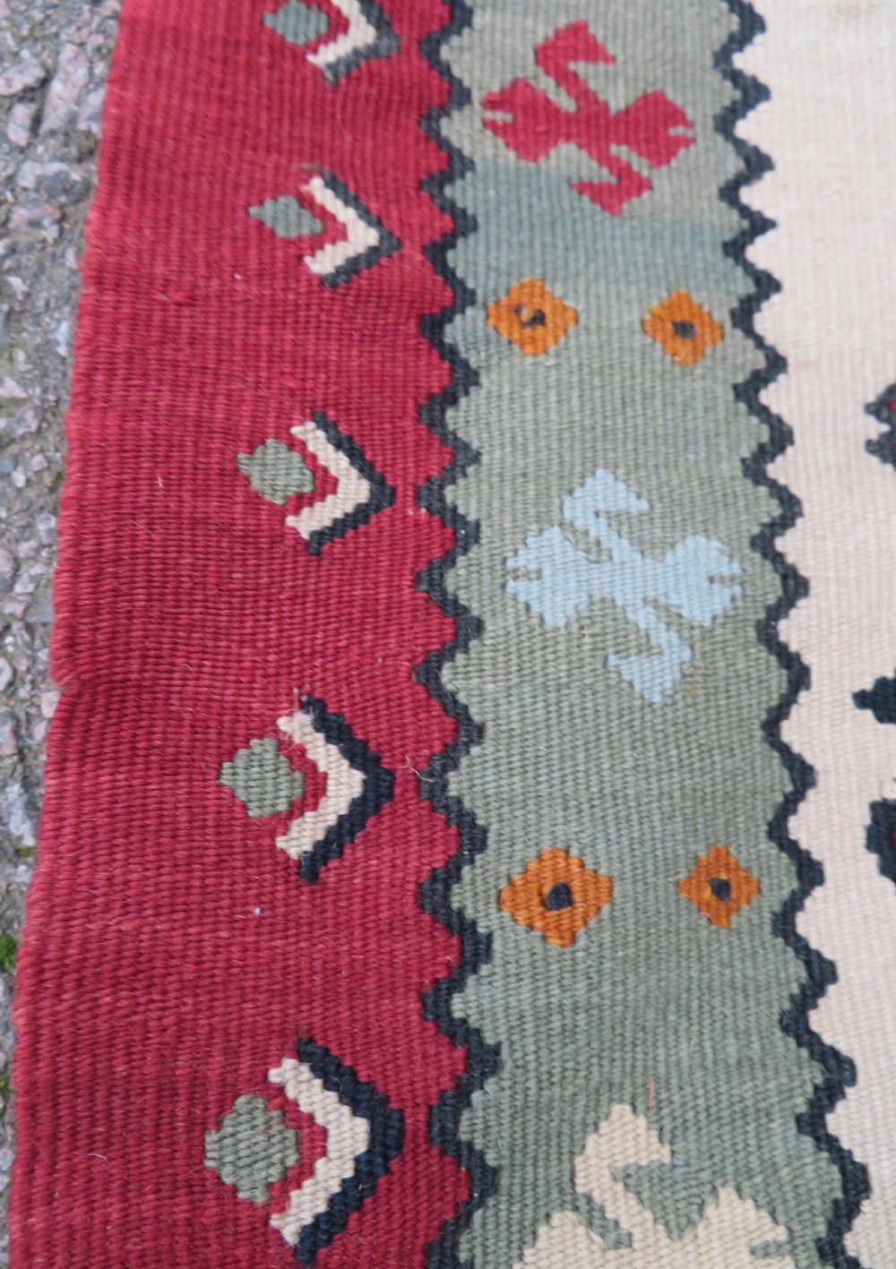 An antique flatweave Bessarabian wool rug featuring a red field with a central black and cream floral medallion, surrounded by a wide floral border and fringed edges. View XV
