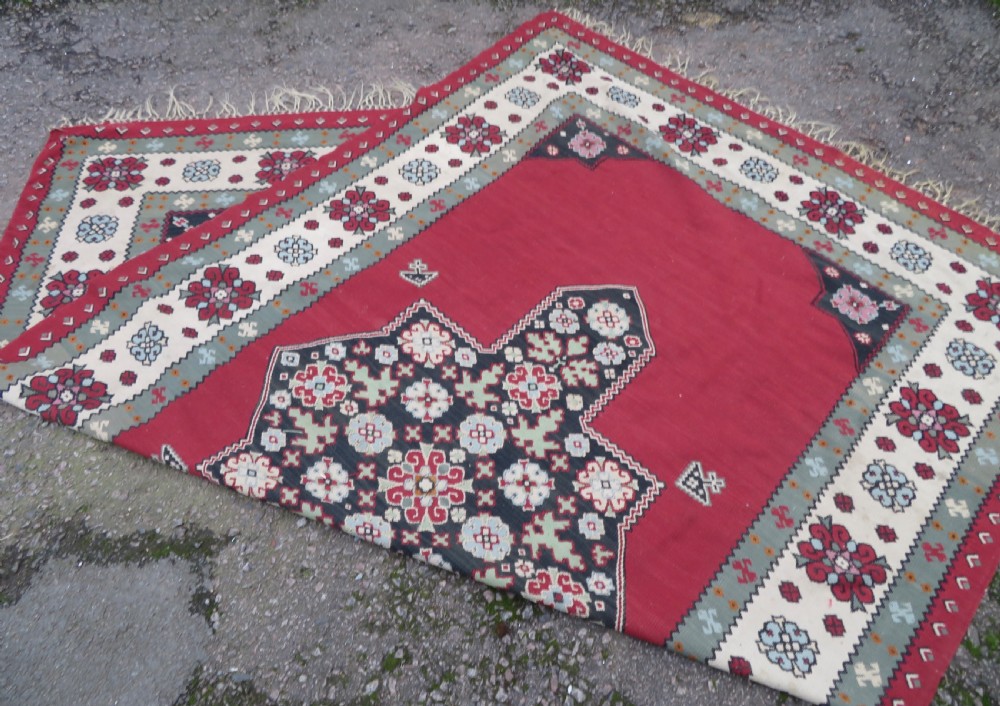 An antique flatweave Bessarabian wool rug featuring a red field with a central black and cream floral medallion, surrounded by a wide floral border and fringed edges. View XVI