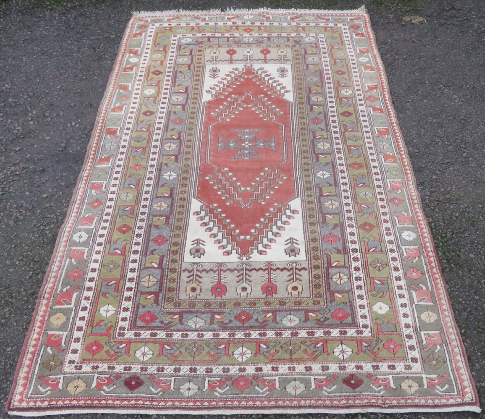 A hand-knotted antique Turkish Melas wool carpet featuring a terracotta red geometric diamond medallion on an ivory field with complex geometric borders.