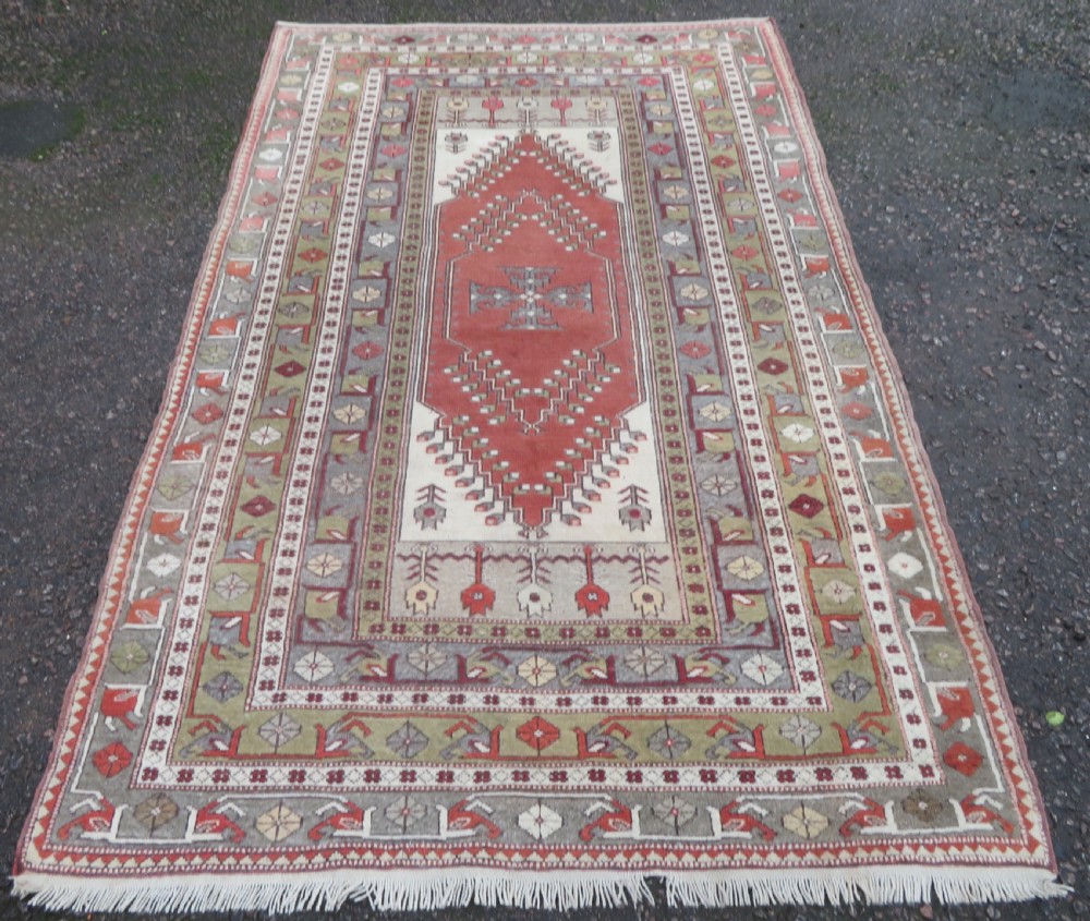 A hand-knotted antique Turkish Melas wool carpet featuring a terracotta red geometric diamond medallion on an ivory field with complex geometric borders. View II