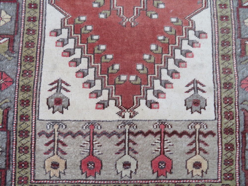 A hand-knotted antique Turkish Melas wool carpet featuring a terracotta red geometric diamond medallion on an ivory field with complex geometric borders. View III