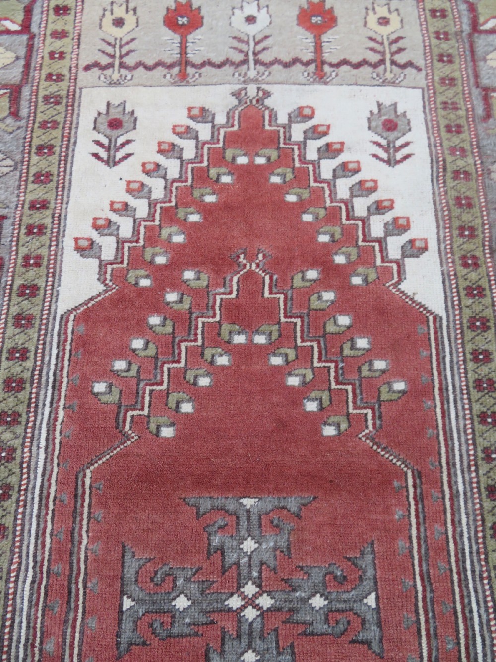 A hand-knotted antique Turkish Melas wool carpet featuring a terracotta red geometric diamond medallion on an ivory field with complex geometric borders. View V
