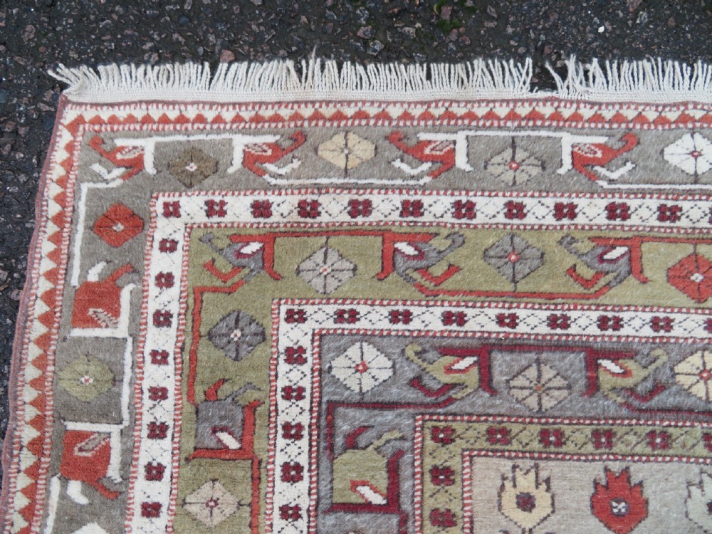 A hand-knotted antique Turkish Melas wool carpet featuring a terracotta red geometric diamond medallion on an ivory field with complex geometric borders. View VI
