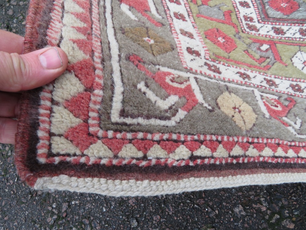 A hand-knotted antique Turkish Melas wool carpet featuring a terracotta red geometric diamond medallion on an ivory field with complex geometric borders. View IX