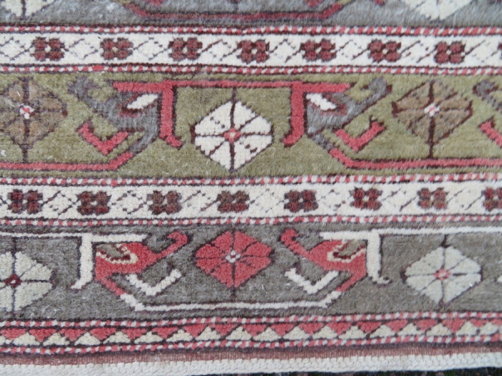 A hand-knotted antique Turkish Melas wool carpet featuring a terracotta red geometric diamond medallion on an ivory field with complex geometric borders. View X