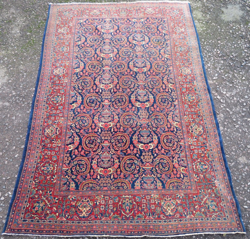 An antique hand-knotted Persian Kashan rug featuring an intricate blue central field with repeating floral urn motifs surrounded by a detailed red multi-banded border. View II