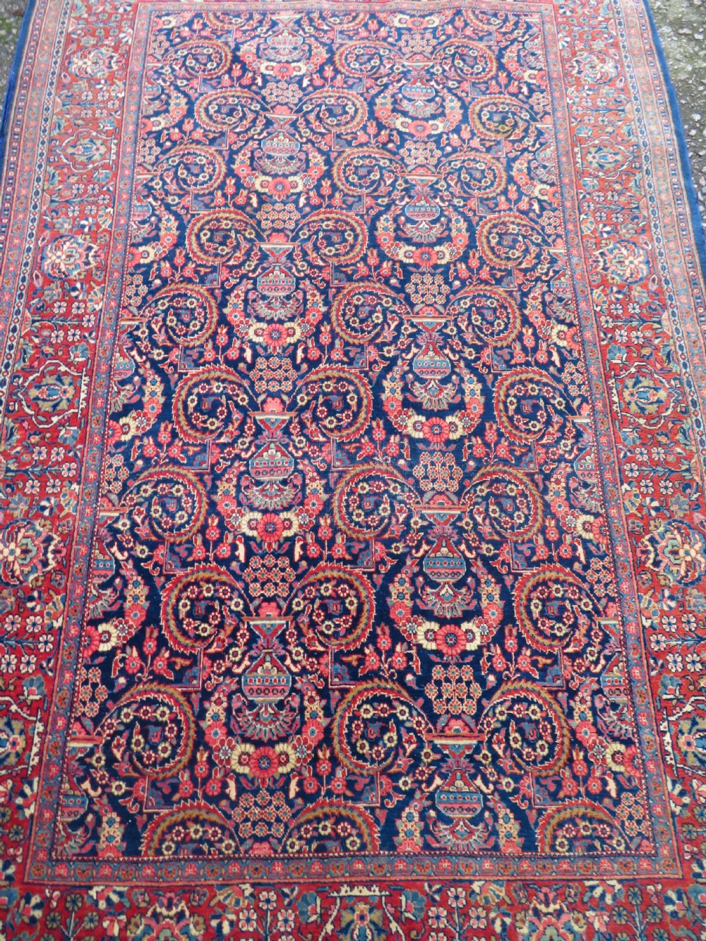 An antique hand-knotted Persian Kashan rug featuring an intricate blue central field with repeating floral urn motifs surrounded by a detailed red multi-banded border. View III