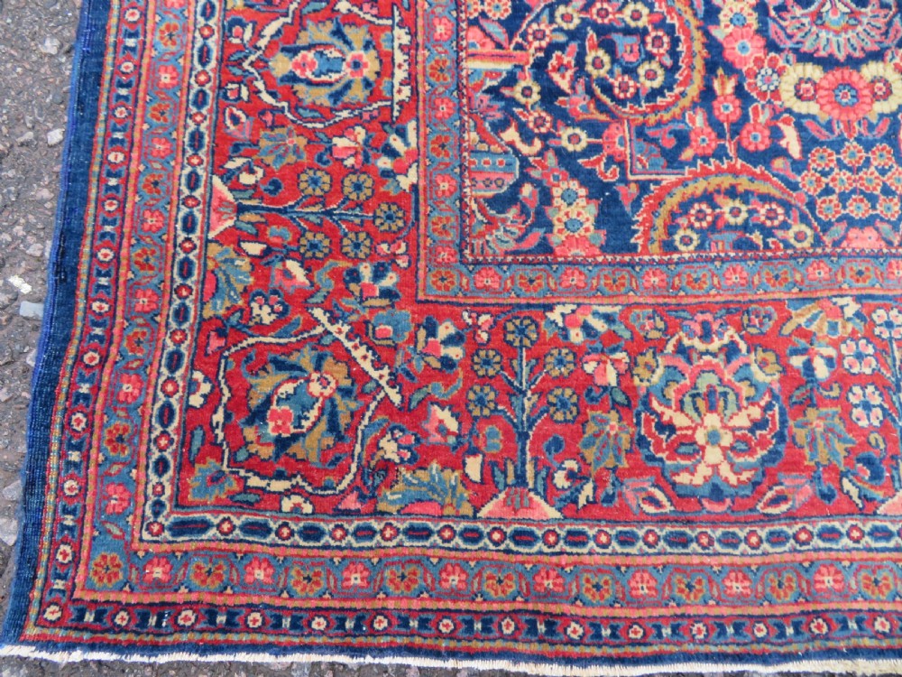 An antique hand-knotted Persian Kashan rug featuring an intricate blue central field with repeating floral urn motifs surrounded by a detailed red multi-banded border. View V