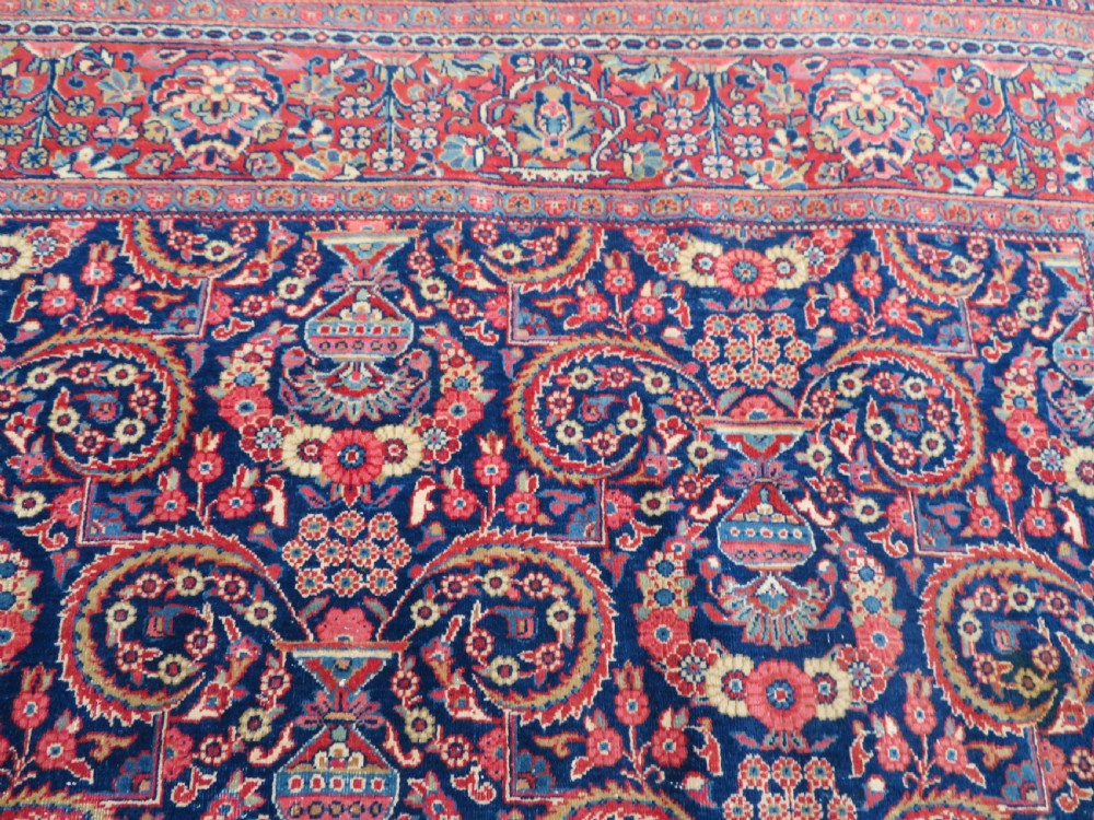 An antique hand-knotted Persian Kashan rug featuring an intricate blue central field with repeating floral urn motifs surrounded by a detailed red multi-banded border. View IX