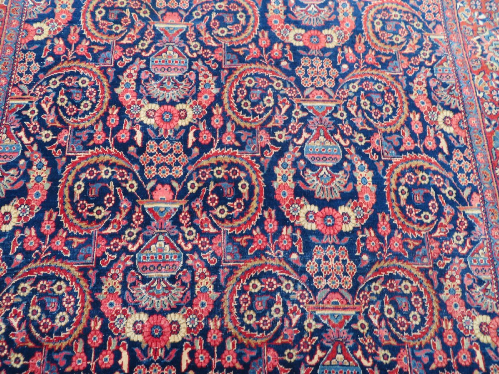 An antique hand-knotted Persian Kashan rug featuring an intricate blue central field with repeating floral urn motifs surrounded by a detailed red multi-banded border. View XI