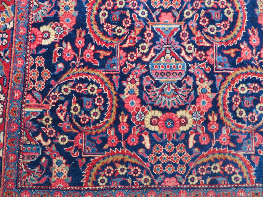 An antique hand-knotted Persian Kashan rug featuring an intricate blue central field with repeating floral urn motifs surrounded by a detailed red multi-banded border. View XII