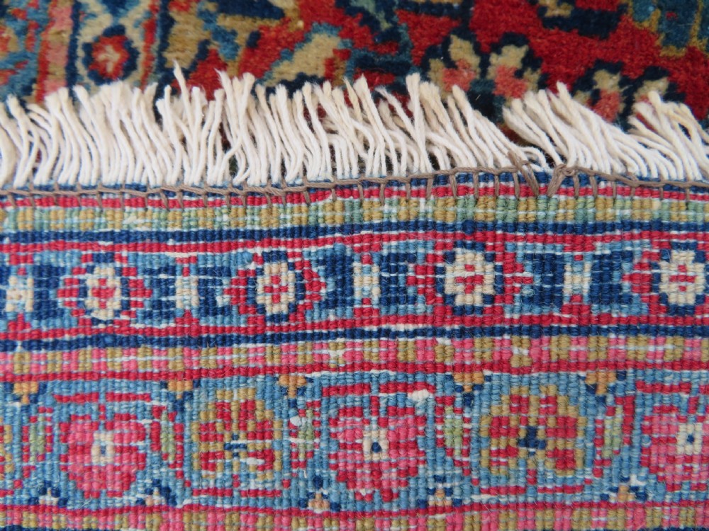 An antique hand-knotted Persian Kashan rug featuring an intricate blue central field with repeating floral urn motifs surrounded by a detailed red multi-banded border. View XIV