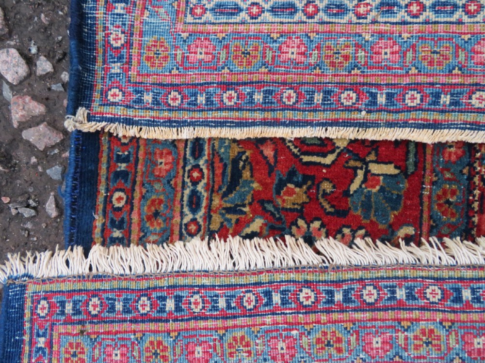 An antique hand-knotted Persian Kashan rug featuring an intricate blue central field with repeating floral urn motifs surrounded by a detailed red multi-banded border. View XV