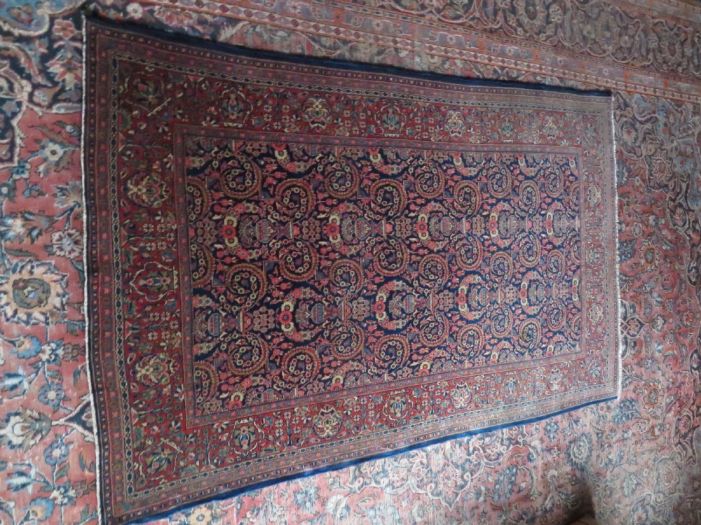 An antique hand-knotted Persian Kashan rug featuring an intricate blue central field with repeating floral urn motifs surrounded by a detailed red multi-banded border. View XVII