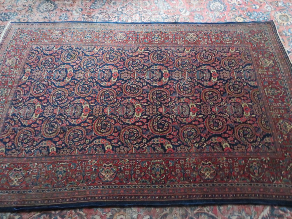 An antique hand-knotted Persian Kashan rug featuring an intricate blue central field with repeating floral urn motifs surrounded by a detailed red multi-banded border. View XVIII