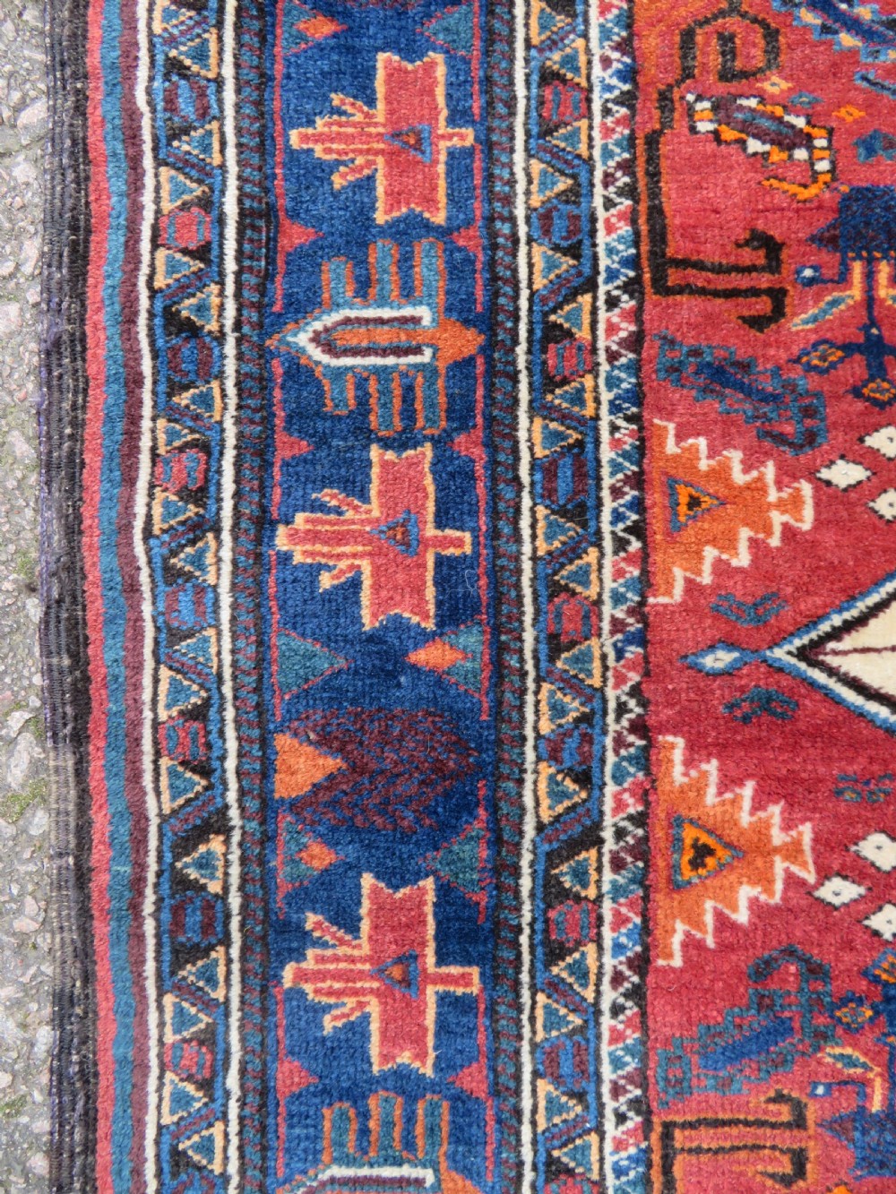 A hand-knotted Baluch wool rug featuring a central stepped dark medallion on a terracotta field bordered by geometric indigo patterns. View V