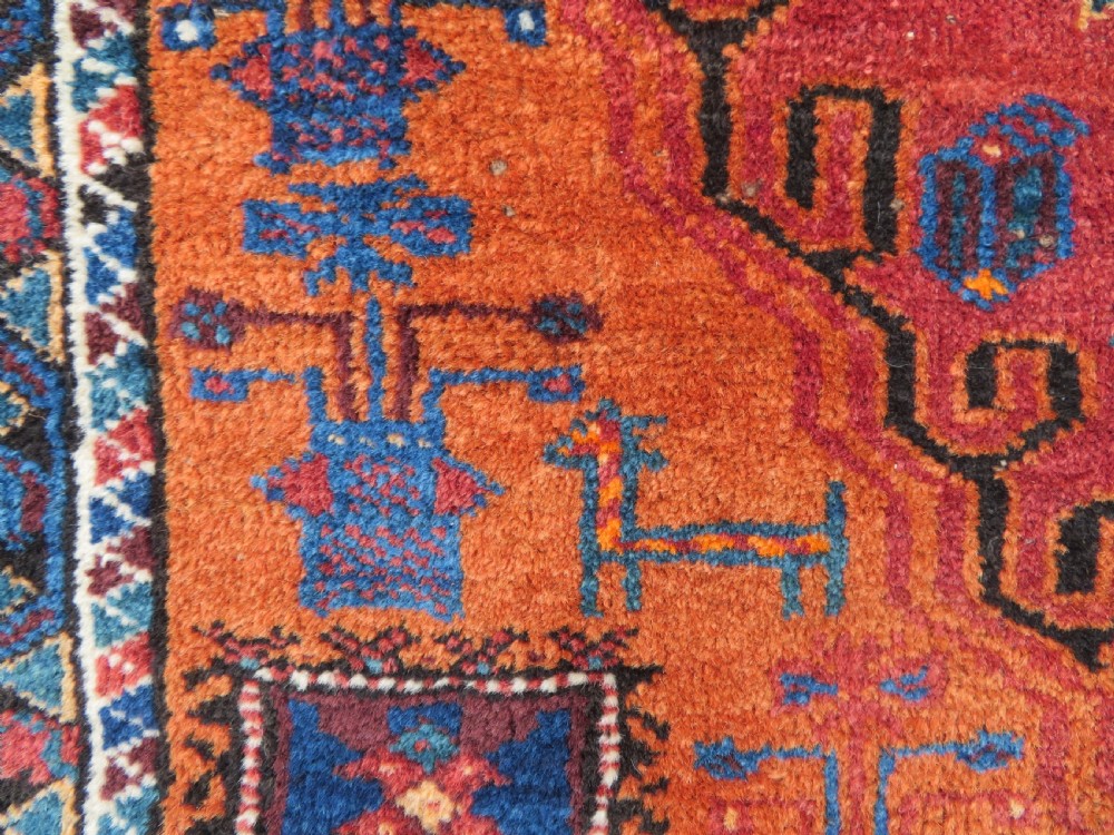 A hand-knotted Baluch wool rug featuring a central stepped dark medallion on a terracotta field bordered by geometric indigo patterns. View VIII