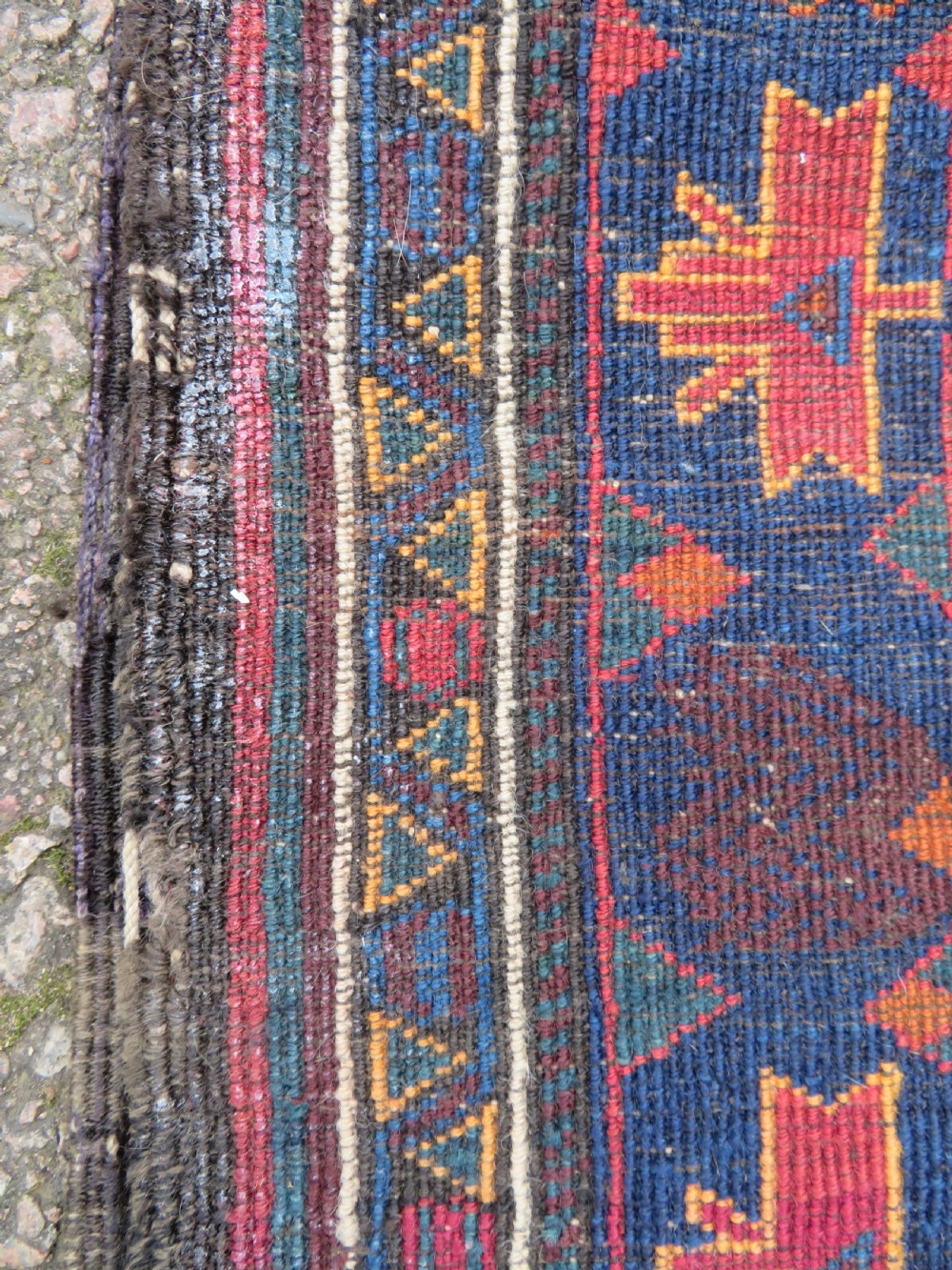 A hand-knotted Baluch wool rug featuring a central stepped dark medallion on a terracotta field bordered by geometric indigo patterns. View XI