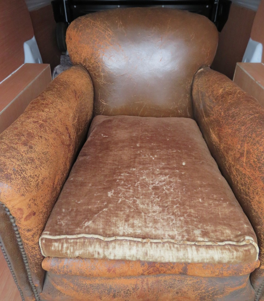A distressed brown leather Art Deco club armchair with brass stud trimming along the rolled arms and a velvet seat cushion. View IV