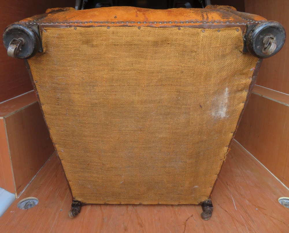 A distressed brown leather Art Deco club armchair with brass stud trimming along the rolled arms and a velvet seat cushion. View V
