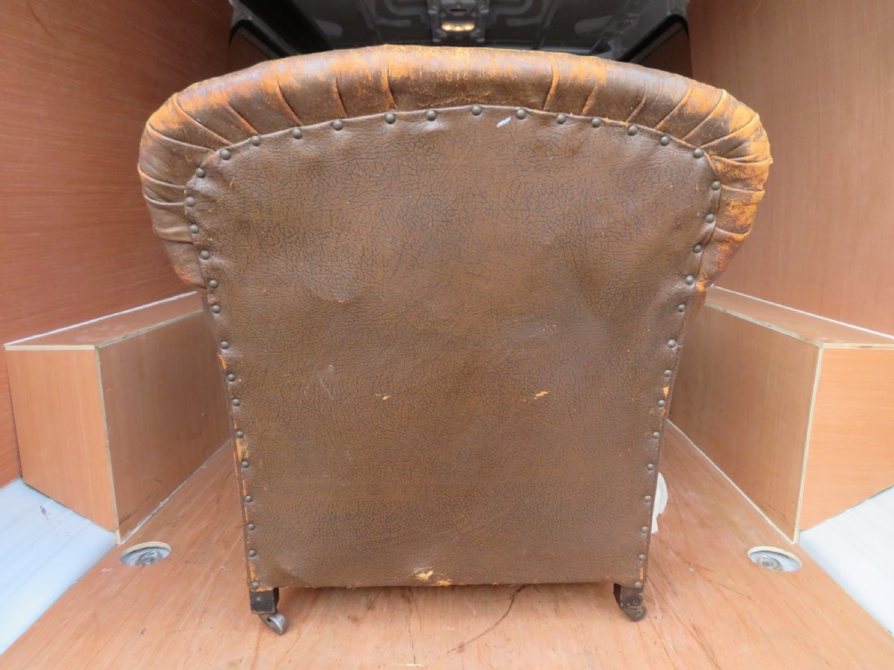 A distressed brown leather Art Deco club armchair with brass stud trimming along the rolled arms and a velvet seat cushion. View VII