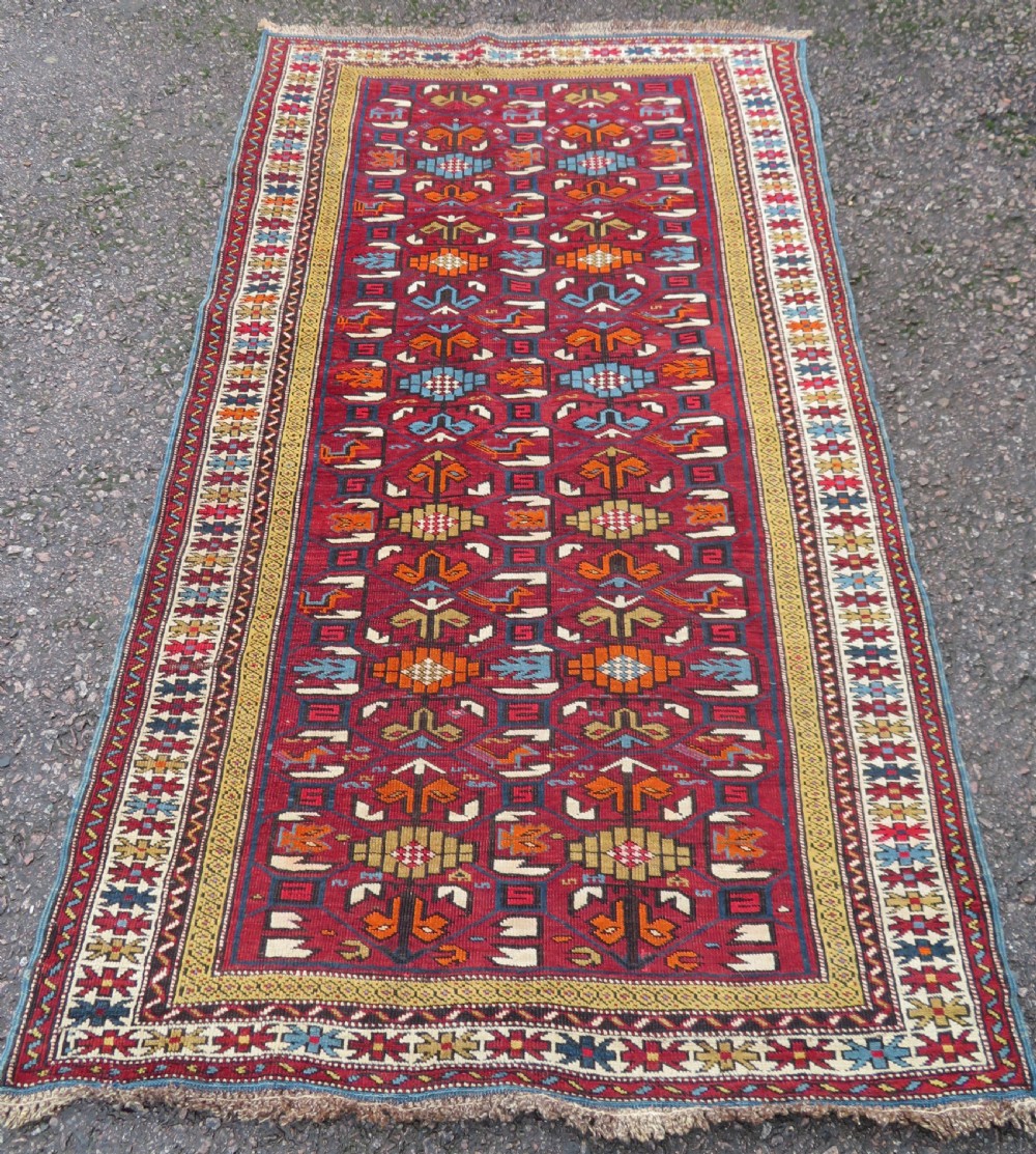 An antique hand-knotted Caucasian Karabagh wool rug featuring a red central field filled with repeating geometric motifs within multi-tiered yellow, blue, and cream borders.