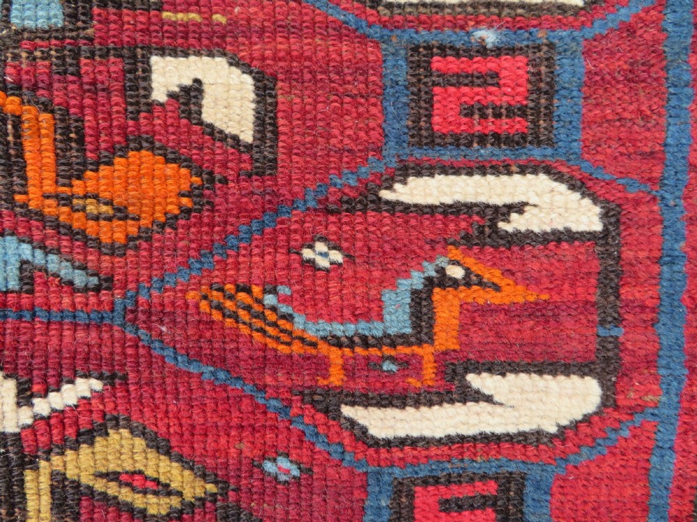 An antique hand-knotted Caucasian Karabagh wool rug featuring a red central field filled with repeating geometric motifs within multi-tiered yellow, blue, and cream borders. View VI