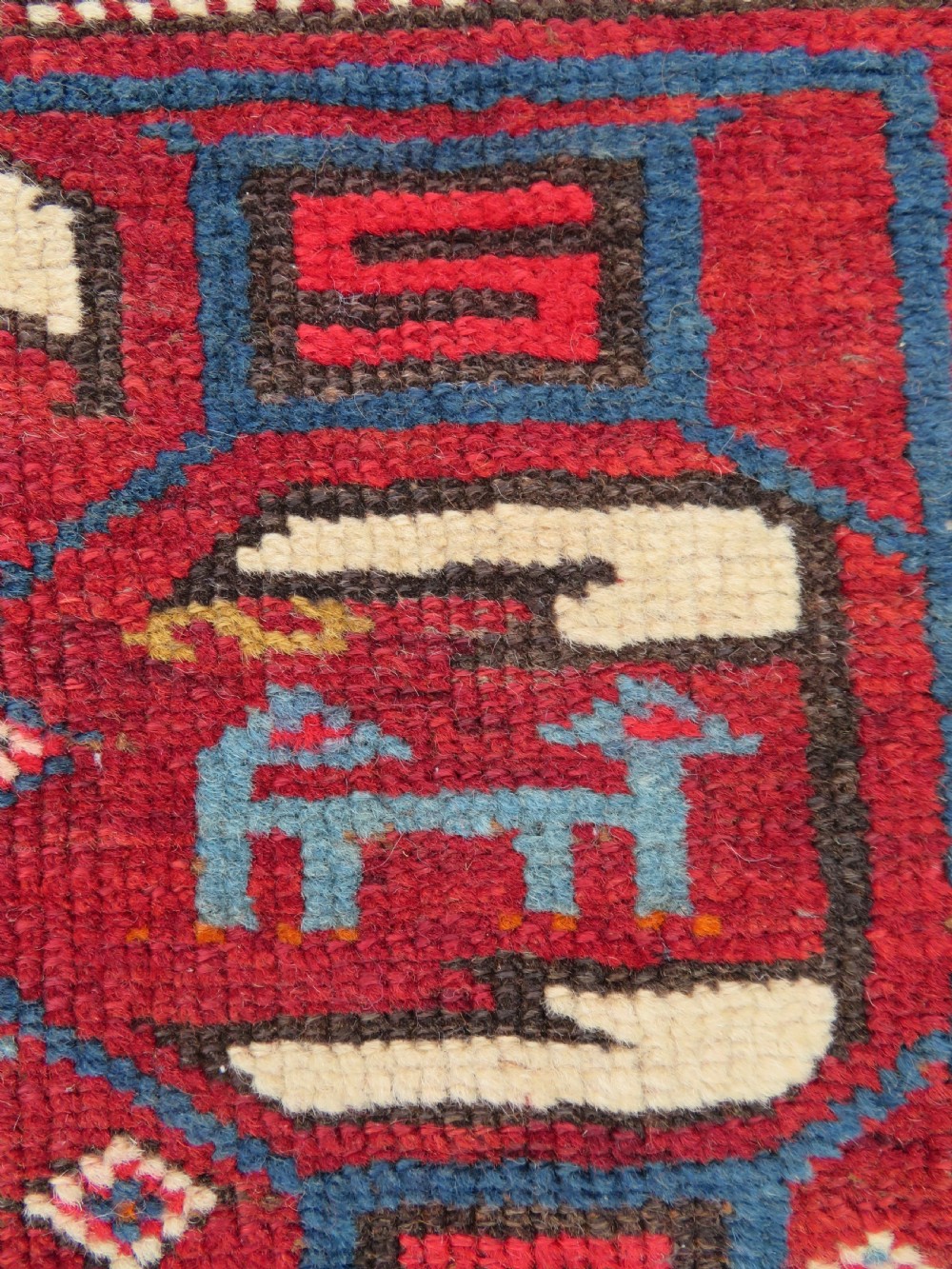 An antique hand-knotted Caucasian Karabagh wool rug featuring a red central field filled with repeating geometric motifs within multi-tiered yellow, blue, and cream borders. View VII