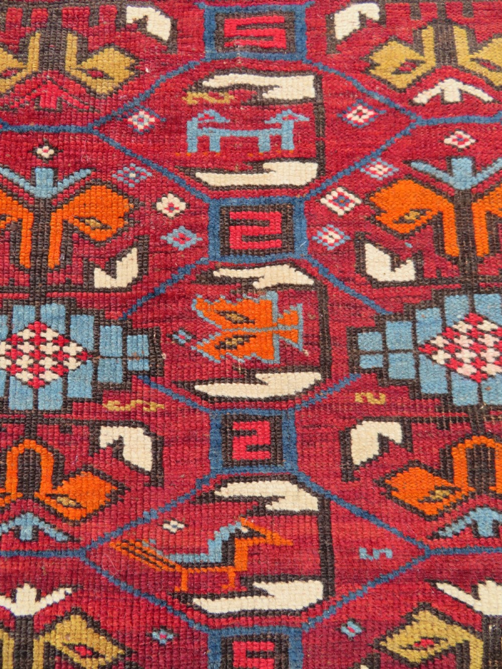An antique hand-knotted Caucasian Karabagh wool rug featuring a red central field filled with repeating geometric motifs within multi-tiered yellow, blue, and cream borders. View VIII