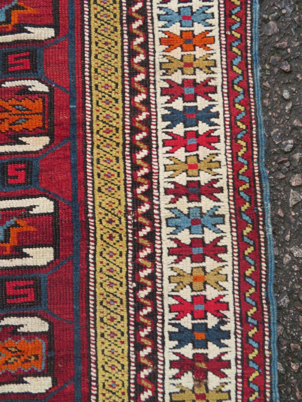 An antique hand-knotted Caucasian Karabagh wool rug featuring a red central field filled with repeating geometric motifs within multi-tiered yellow, blue, and cream borders. View IX