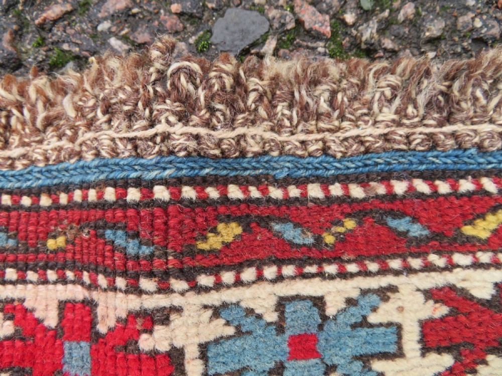 An antique hand-knotted Caucasian Karabagh wool rug featuring a red central field filled with repeating geometric motifs within multi-tiered yellow, blue, and cream borders. View X