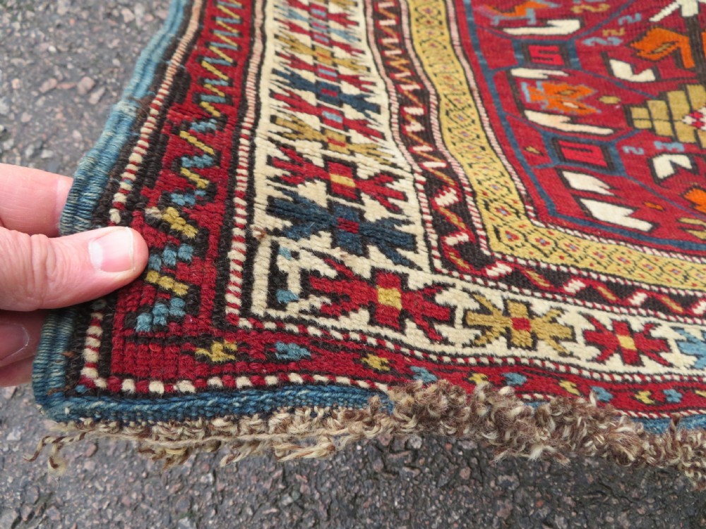 An antique hand-knotted Caucasian Karabagh wool rug featuring a red central field filled with repeating geometric motifs within multi-tiered yellow, blue, and cream borders. View XI