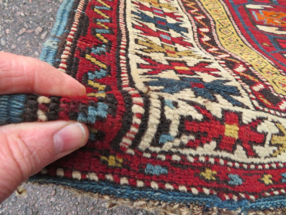 An antique hand-knotted Caucasian Karabagh wool rug featuring a red central field filled with repeating geometric motifs within multi-tiered yellow, blue, and cream borders. View XII