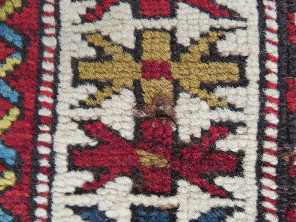 An antique hand-knotted Caucasian Karabagh wool rug featuring a red central field filled with repeating geometric motifs within multi-tiered yellow, blue, and cream borders. View XIII