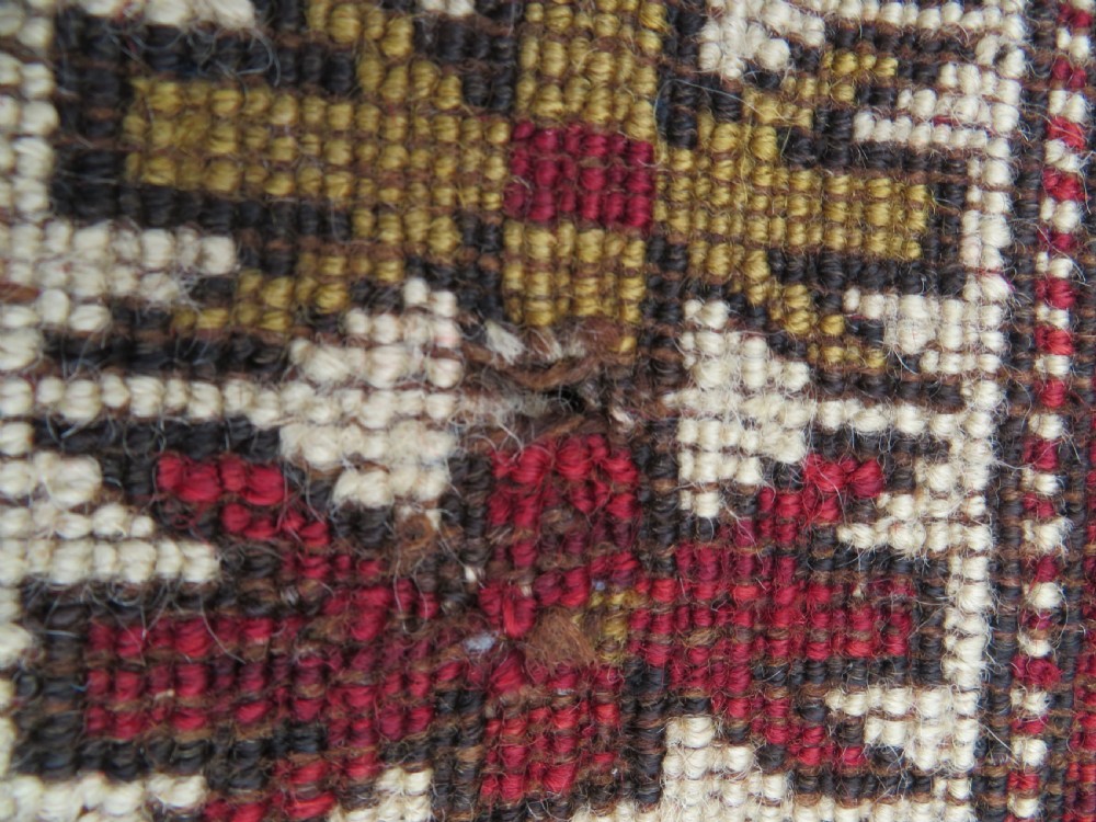 An antique hand-knotted Caucasian Karabagh wool rug featuring a red central field filled with repeating geometric motifs within multi-tiered yellow, blue, and cream borders. View XIV