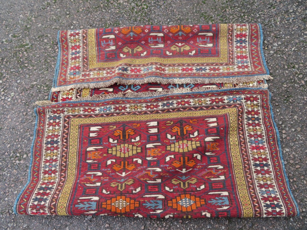 An antique hand-knotted Caucasian Karabagh wool rug featuring a red central field filled with repeating geometric motifs within multi-tiered yellow, blue, and cream borders. View XV