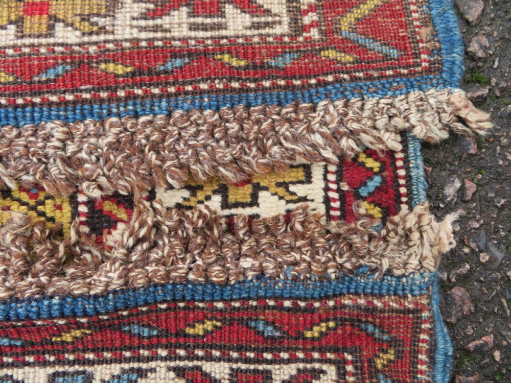 An antique hand-knotted Caucasian Karabagh wool rug featuring a red central field filled with repeating geometric motifs within multi-tiered yellow, blue, and cream borders. View XVI