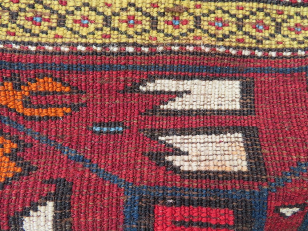 An antique hand-knotted Caucasian Karabagh wool rug featuring a red central field filled with repeating geometric motifs within multi-tiered yellow, blue, and cream borders. View XVII