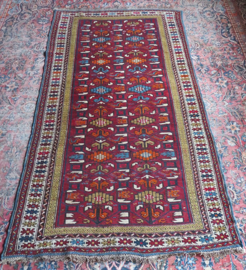 An antique hand-knotted Caucasian Karabagh wool rug featuring a red central field filled with repeating geometric motifs within multi-tiered yellow, blue, and cream borders. View XVIII