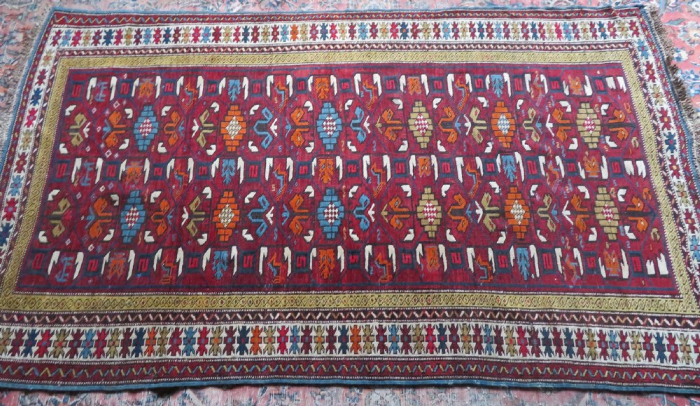 An antique hand-knotted Caucasian Karabagh wool rug featuring a red central field filled with repeating geometric motifs within multi-tiered yellow, blue, and cream borders. View XIX