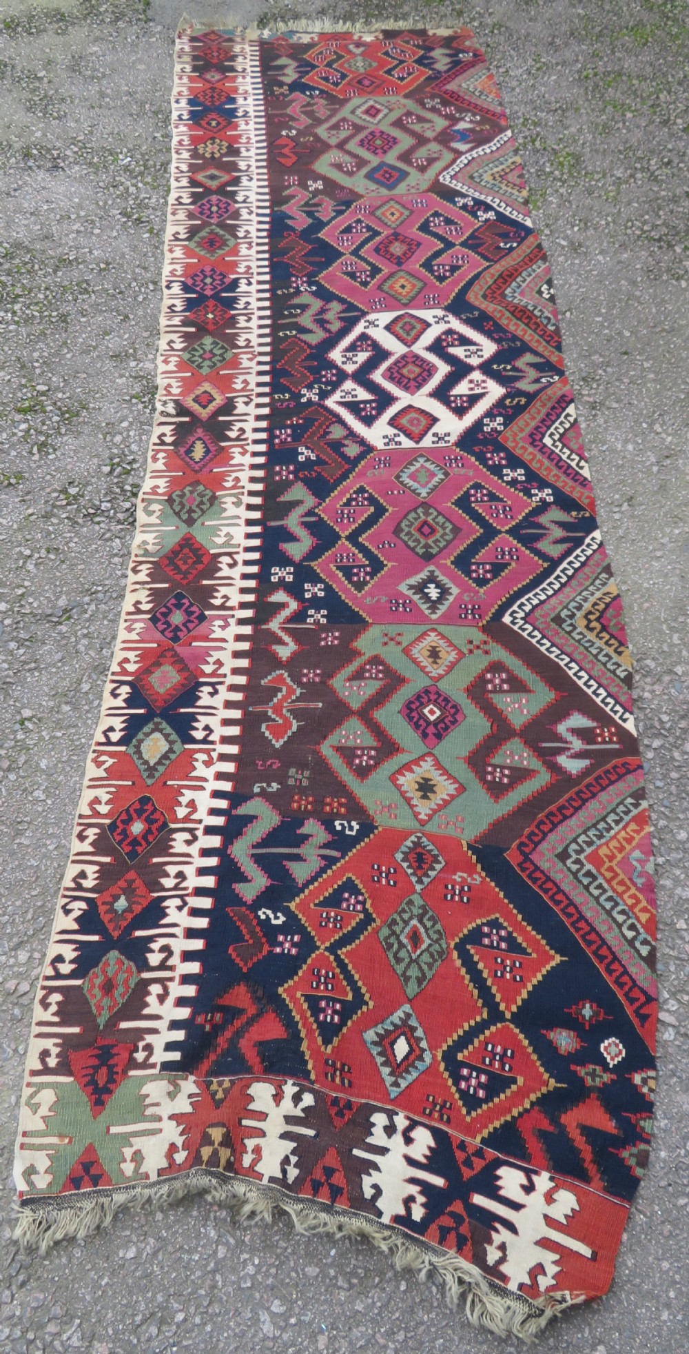 A long handwoven Turkish flatweave Kilim runner featuring intricate geometric diamond medallions in red, navy blue, green, and cream.