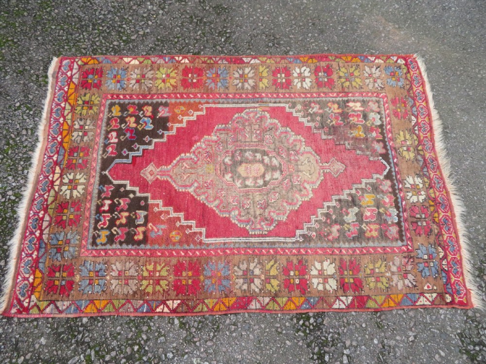 An antique hand-knotted Turkish Mujur wool rug featuring a stepped central medallion on a red field with patterned borders and fringed edges. View II