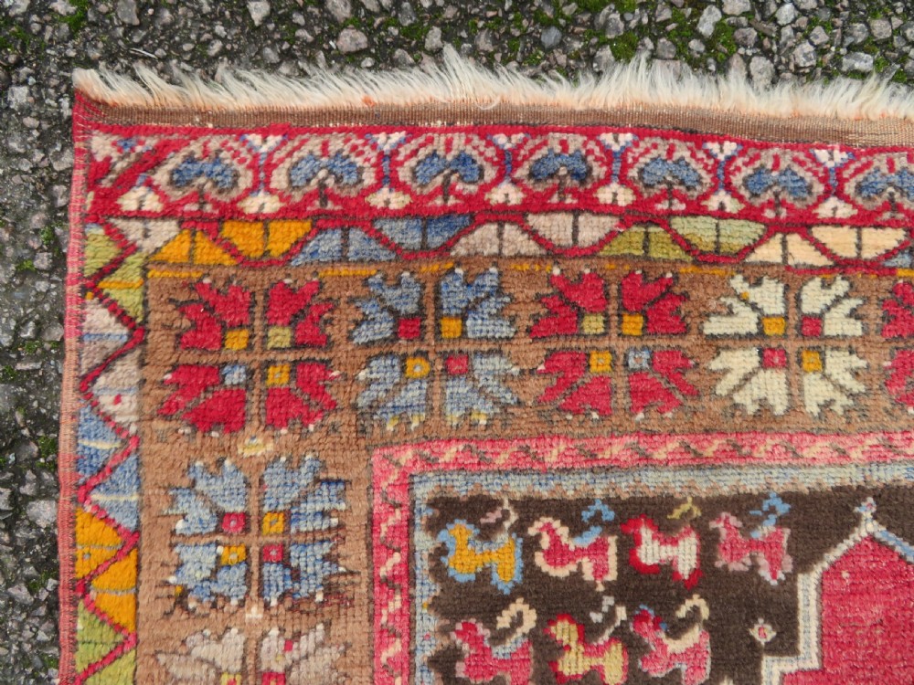 An antique hand-knotted Turkish Mujur wool rug featuring a stepped central medallion on a red field with patterned borders and fringed edges. View III