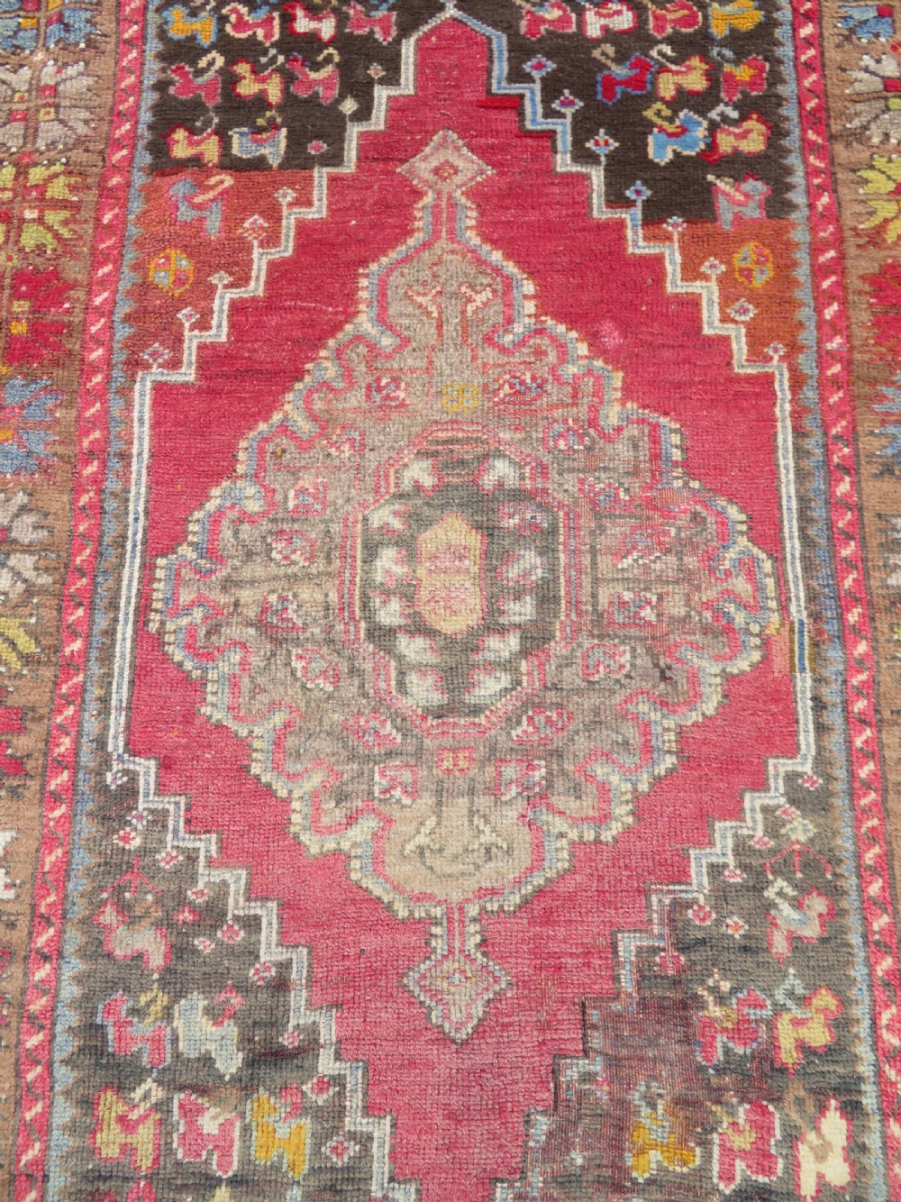 An antique hand-knotted Turkish Mujur wool rug featuring a stepped central medallion on a red field with patterned borders and fringed edges. View IV